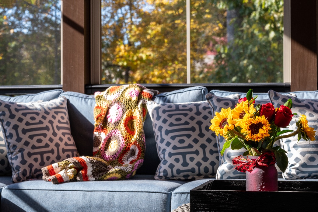 Nice blue couch on a screened patio with fresh flowers on a table.